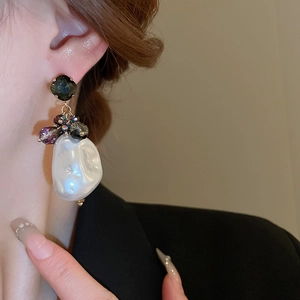 Detailed close-up of Baroque pearl earrings with green gemstones and golden accents