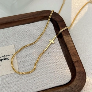 Detail shot of a minimalist gold cross pendant on a delicate curb chain jewelry piece
