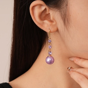 Close-up of elegant gold drop earrings with purple faceted crystals and round violet pearls