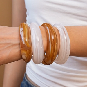 Close-up of four chunky acrylic bangles in amber and milky white marble patterns