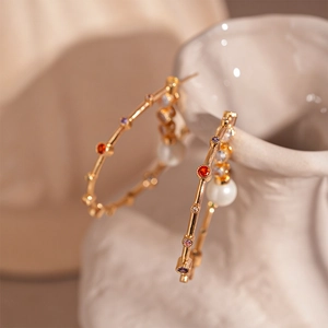 Detail of gold bamboo hoop earrings with colorful zircon stones and large pearl accents