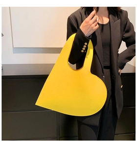 Detail of a bright yellow heart-shaped leather handbag styled with a black suit