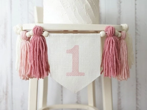 Close-up of pink tassel banner with embroidered number one on a wooden bead baby highchair