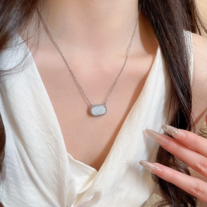 Close-up of minimalist silver oval pendant necklace worn on a white V-neck top