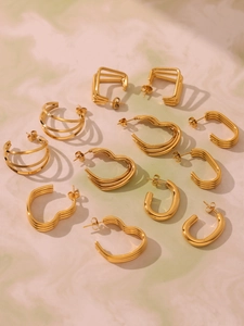 Detailed close-up of golden U-shaped earrings with textured layered lines on marble base