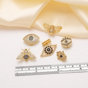 Macro shot of evil eye and bee charms in gold-plated stainless steel with zircon inlay