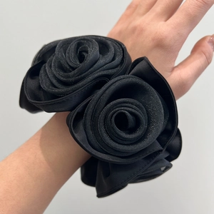 Detail of a large black rose fabric scrunchie with layered satin folds worn on a wrist