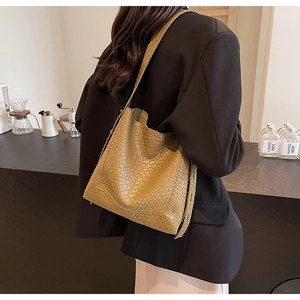 Detail of khaki woven bucket bag on shoulder in a cozy coffee shop setting