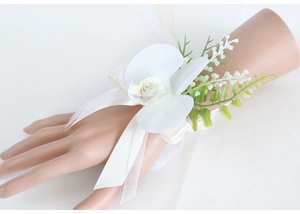 Elegant white orchid wrist corsage with silk ribbon and greenery for wedding guests