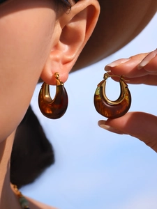 Close-up of golden hoop earrings with amber resin inlay worn against a clear blue sky