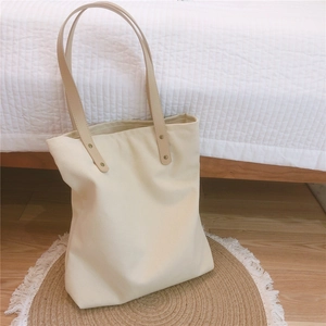 Detail of sturdy cream canvas tote bag with brown leather straps and metal rivets