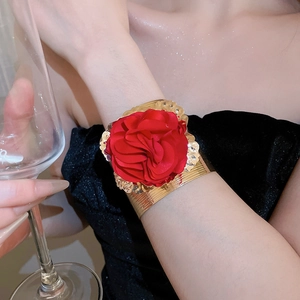 Golden metal cuff bracelet with a large red fabric rose flower on a model wrist