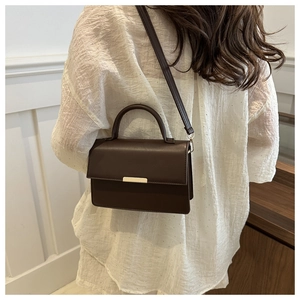 Détail du sac bandoulière en cuir marron foncé avec boucle dorée porté par un mannequin