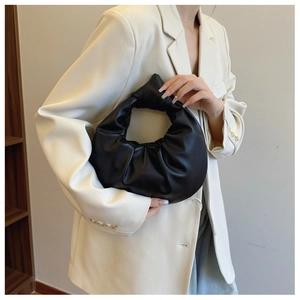 Close-up of black pleated dumpling bag with a knotted handle detail on light blazer