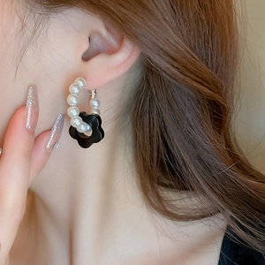 Detailed view of pearl hoop earrings with a black resin flower drop on a model