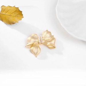 Detailed view of golden bow brooch with brushed texture and elegant pearl inlay
