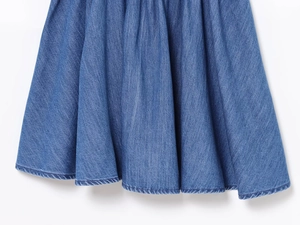 Dettaglio dell'orlo del vestito in denim blu con cuciture precise e trama del tessuto