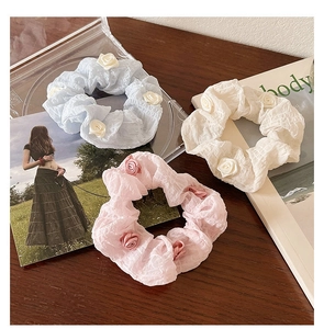 Flat lay of camellia hair scrunchies in blue, beige, and pink on a dark wood background