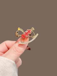 Detail of a gold rocking horse brooch with red enamel dots and shimmering rhinestones