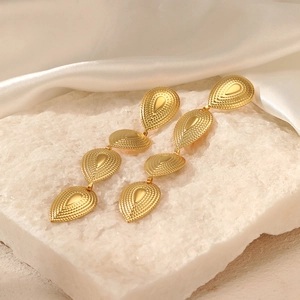 Gold teardrop dangle earrings with radial texture on elegant white silk and crystal