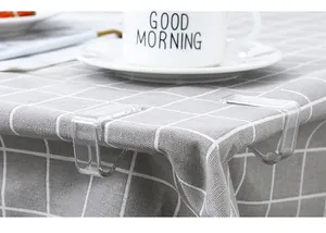 Close-up of clear plastic tablecloth clips in use on a grey checkered table cloth