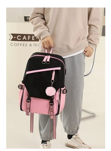 Detail of a black and pink patchwork school backpack with a pink fluffy ball pendant