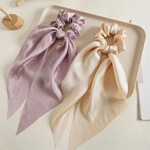 Detail of purple and beige satin scrunchies with long ribbons on a minimalist tray