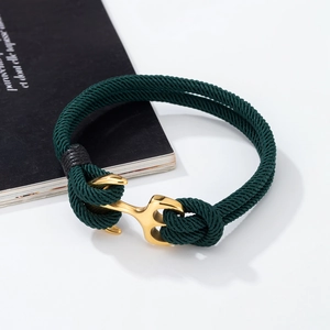 Detail of dark green woven nautical bracelet with a gold anchor clasp on a white background