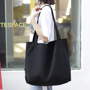 Minimalist black large capacity canvas tote bag worn by a model in natural street light