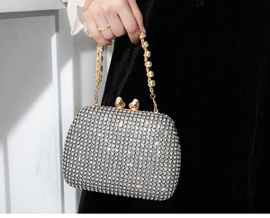 Detail of silver rhinestone evening bag featuring a gold heart-shaped metal clasp and chain