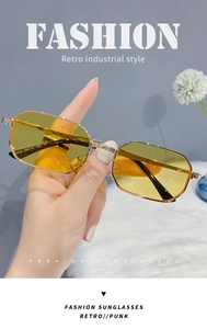 Detail view of gold metal polygon sunglasses with yellow lenses held by a model