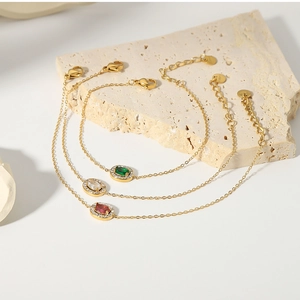 Three gold stainless steel bracelets with red, green, and clear zircon charms on stone