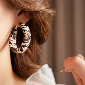 Macro side view of a large leopard print leather hoop earring worn by a model