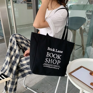 Outdoor shot of a black canvas tote bag with Brick Lane Book Shop print on white T-shirt