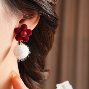 Close-up of burgundy flocked flower earrings with white plush ball on female model