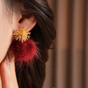Close-up of zircon fireworks earrings with deep red plush pom poms on a model