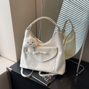 Grande borsa tote crema con dettaglio fiocco e ciondolo a nuvola su tavolo scuro