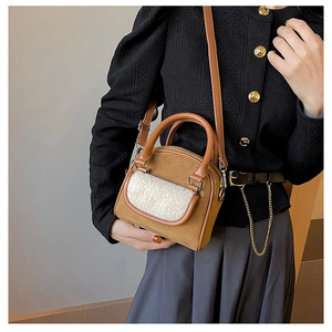 Detail of a brown suede and white faux fur patchwork handbag held by a model