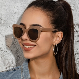Detail view of khaki cat-eye sunglasses with oversized frames and dark lenses on model