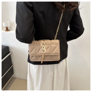 Detail of beige quilted shoulder bag featuring gold S-logo, tassel and chain strap