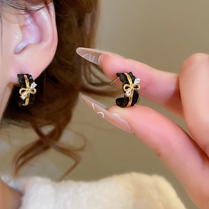Detail of 18k gold plated C-shaped earrings with black bow design and clear crystals