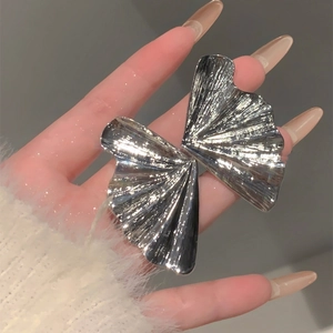 Silver metallic fan-shaped heart earrings with pleated texture shown on hand