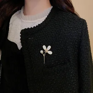 Détail de la broche fleur dorée avec pétales en nacre et perle sur une veste en tweed