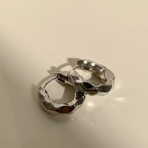 Macro shot of silver metal earrings with irregular liquid texture and wave pattern