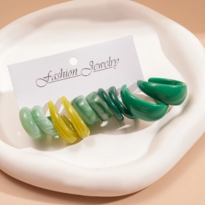 Set of six pairs of green resin geometric earrings displayed on a white tray