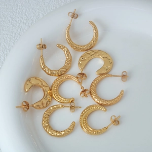Fashionable golden stainless steel C-shaped hoop earrings with varied textures on white plate