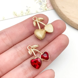 Macro detail of cherry pendants with red heart crystals and golden leaves for jewelry making