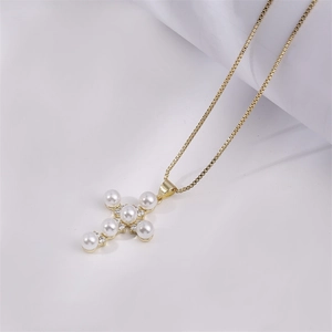 Gold cross pendant necklace featuring inlaid pearls and rhinestones on a white fabric
