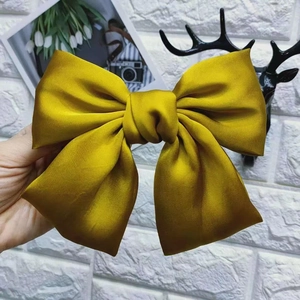 Detailed view of a golden satin bow hair clip held by hand against a white wall