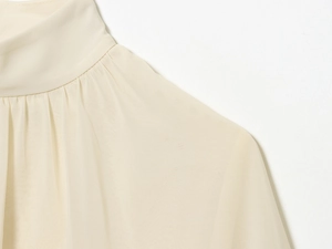 Close-up of the elegant standing collar and pleated shoulder details of the beige blouse